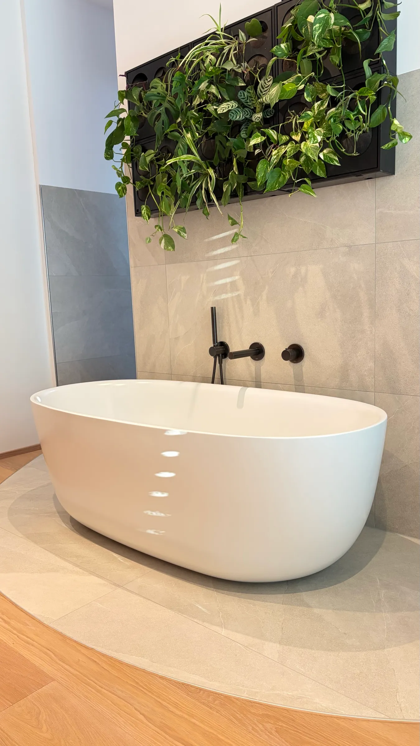 Freistehende Badewanne auf einer Fliesen-Insel im Parkett, darüber eine Pflanzenwand